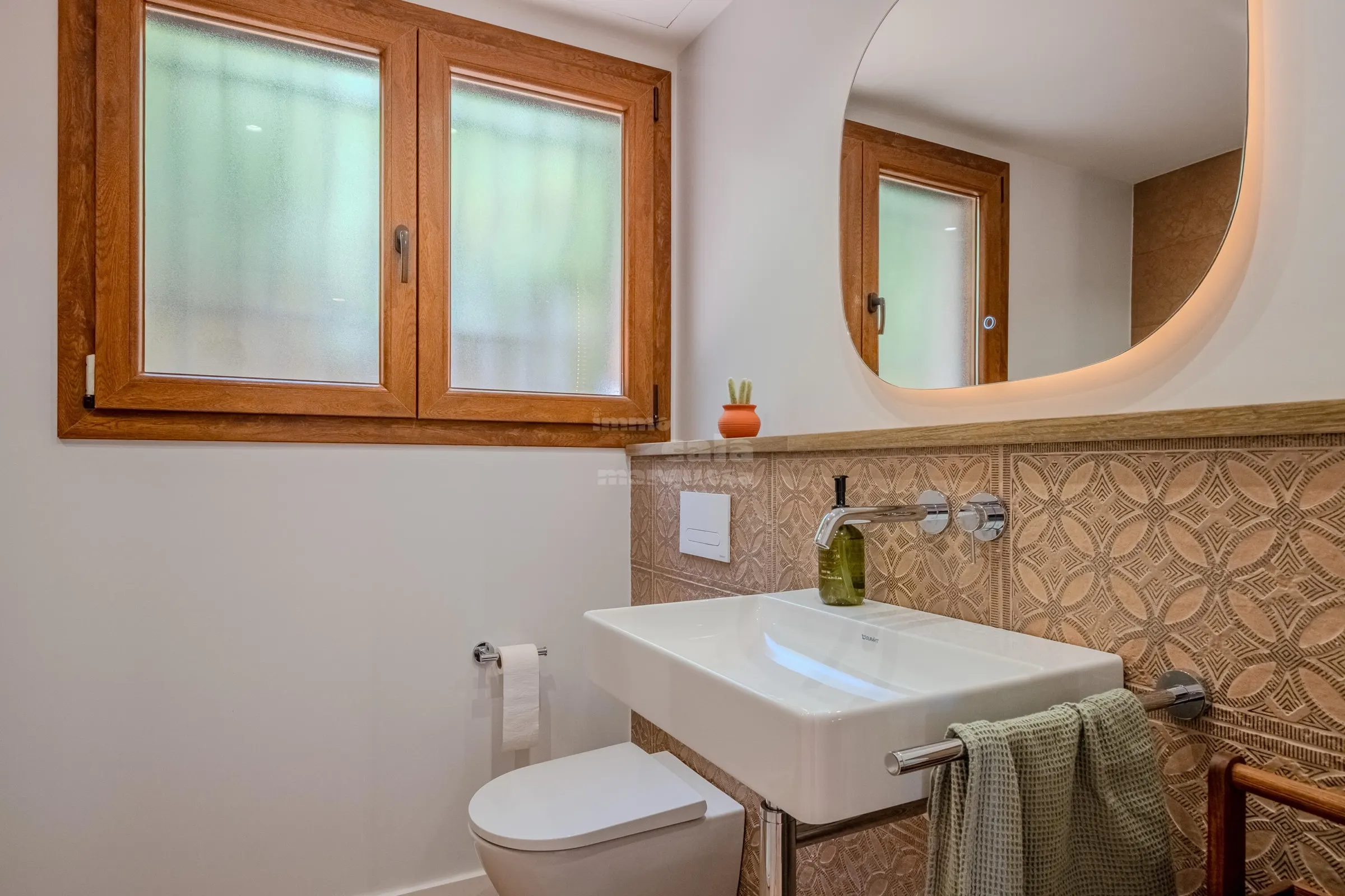 Guest bathroom with embossed terracotta tiling, floating basin and backlit oval mirror