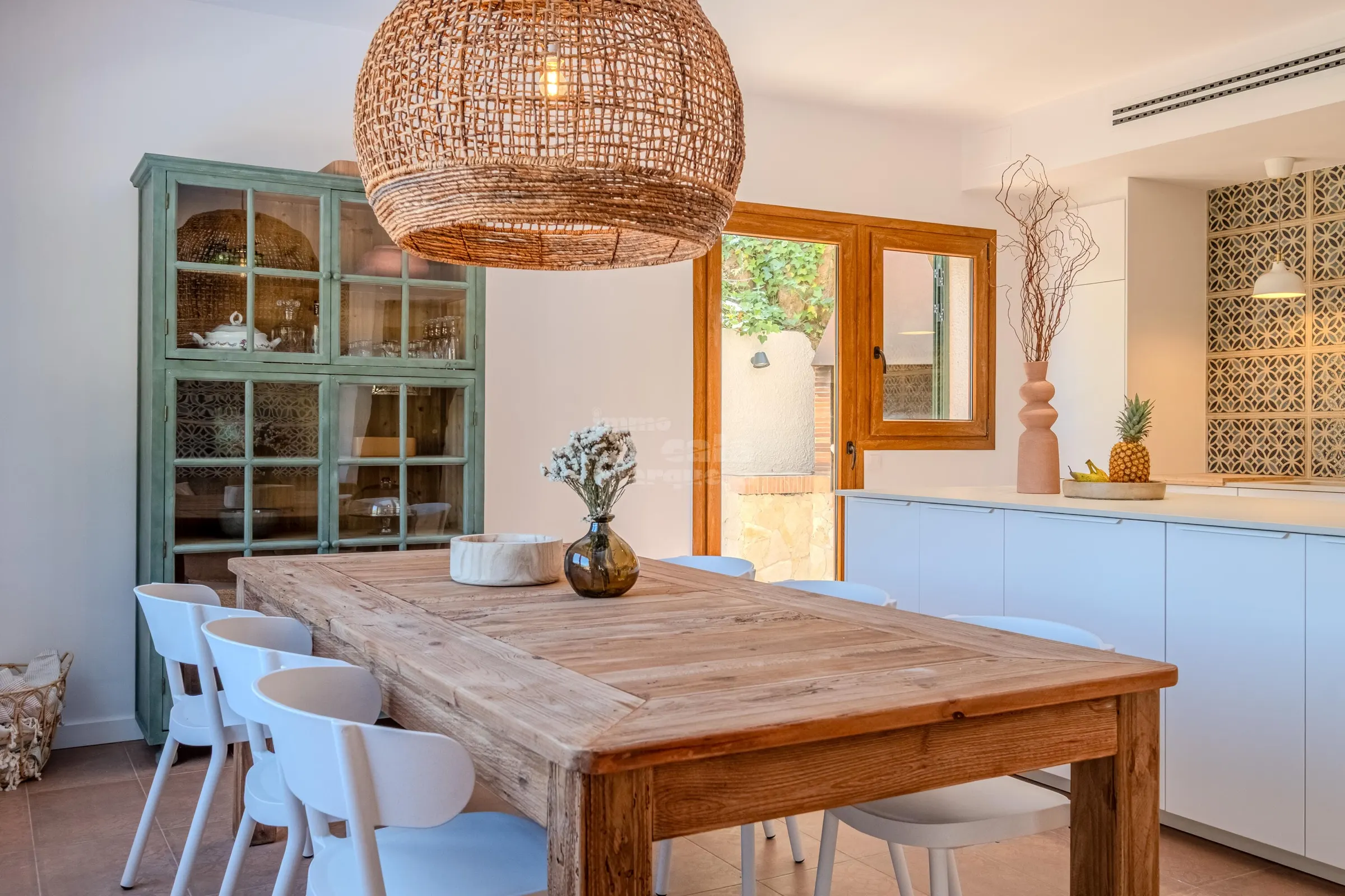 Farmhouse dining table for eight under a rattan pendant, beside a vintage green cabinet