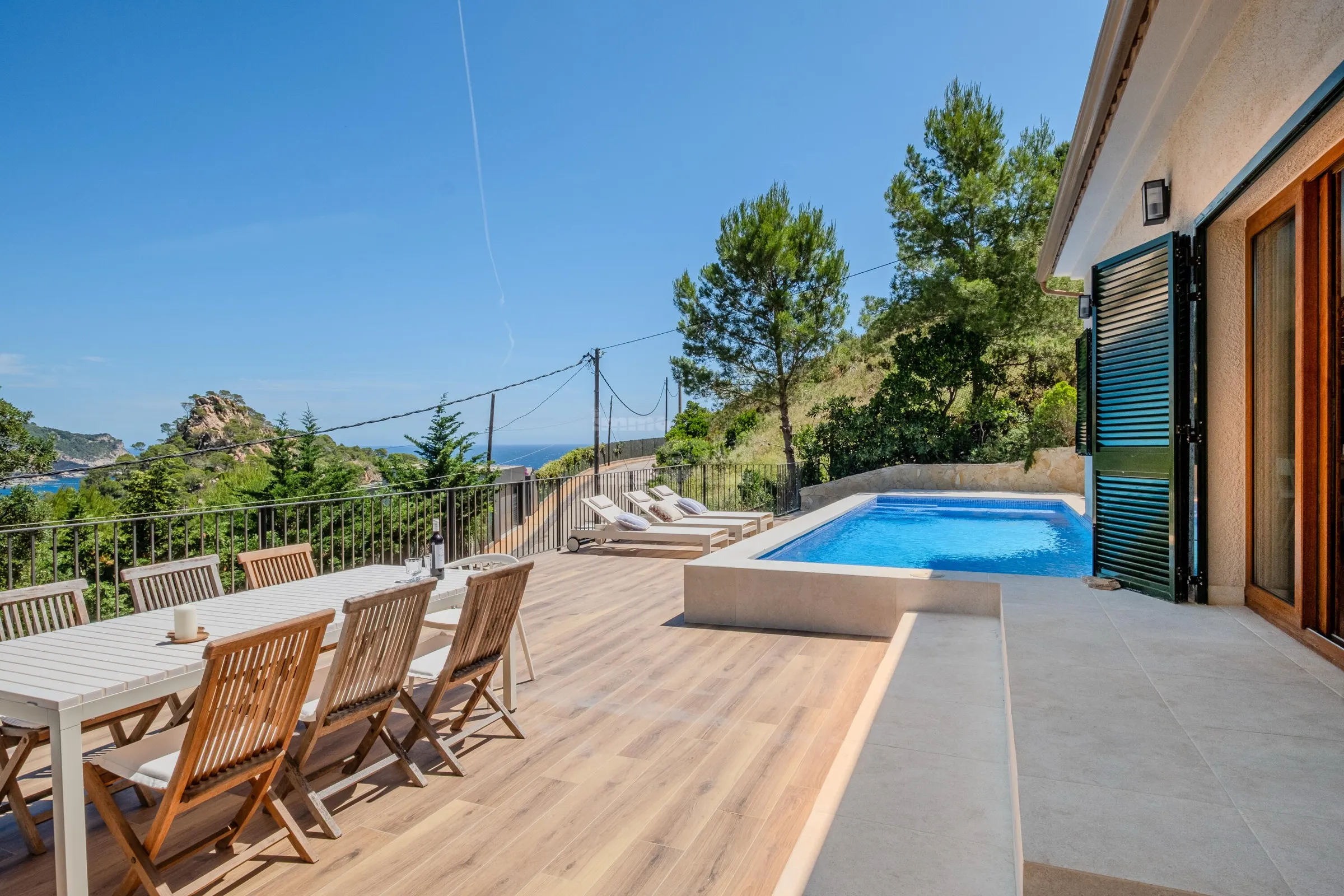 Sun-drenched terrace of Casa Aurora with a long wooden dining table, private pool and the sea beyond