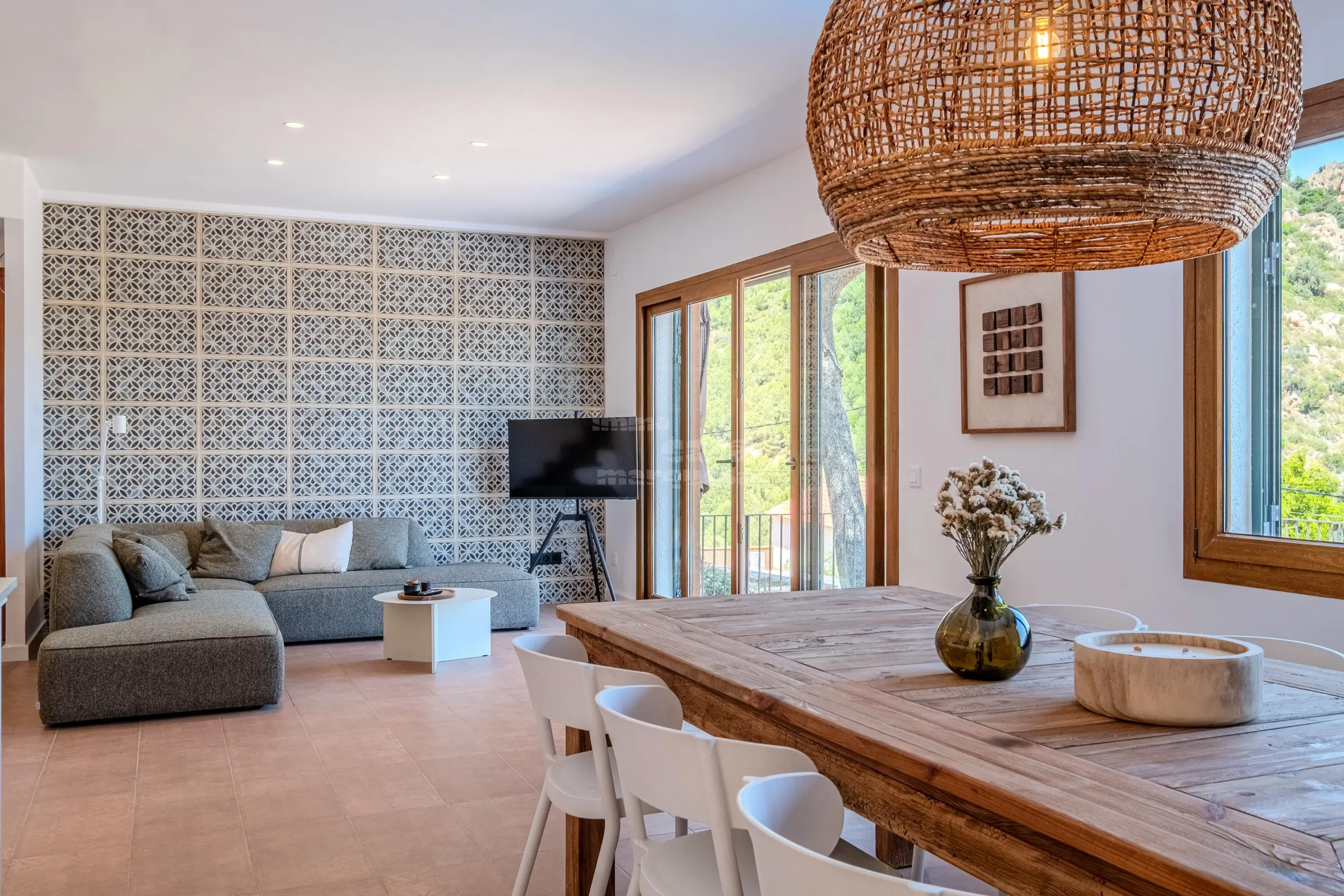 Open-plan living room with patterned tile wall, grey sofa and rattan pendant over the dining table